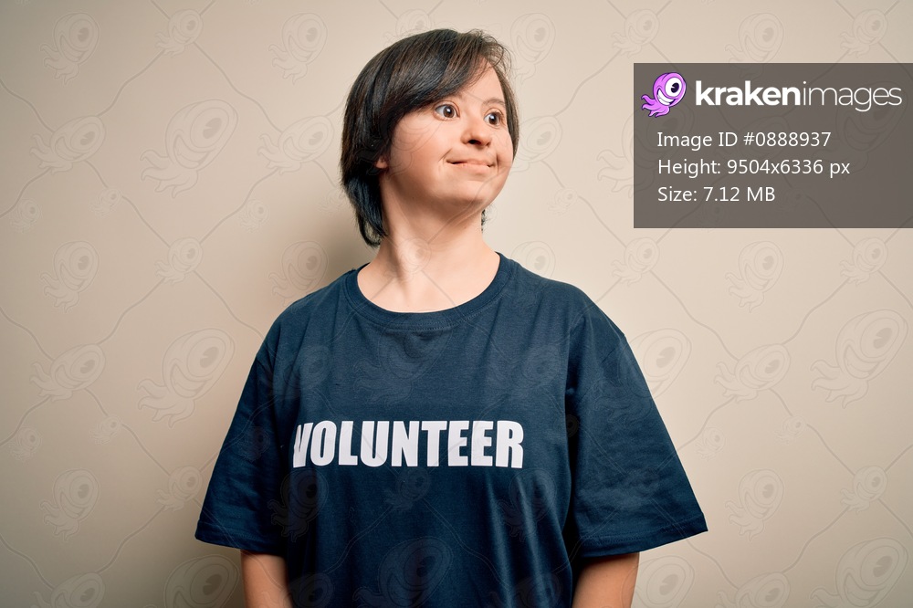 Young down syndrome volunteer woman wearing social care charity t-shirt smiling looking to the side and staring away thinking.