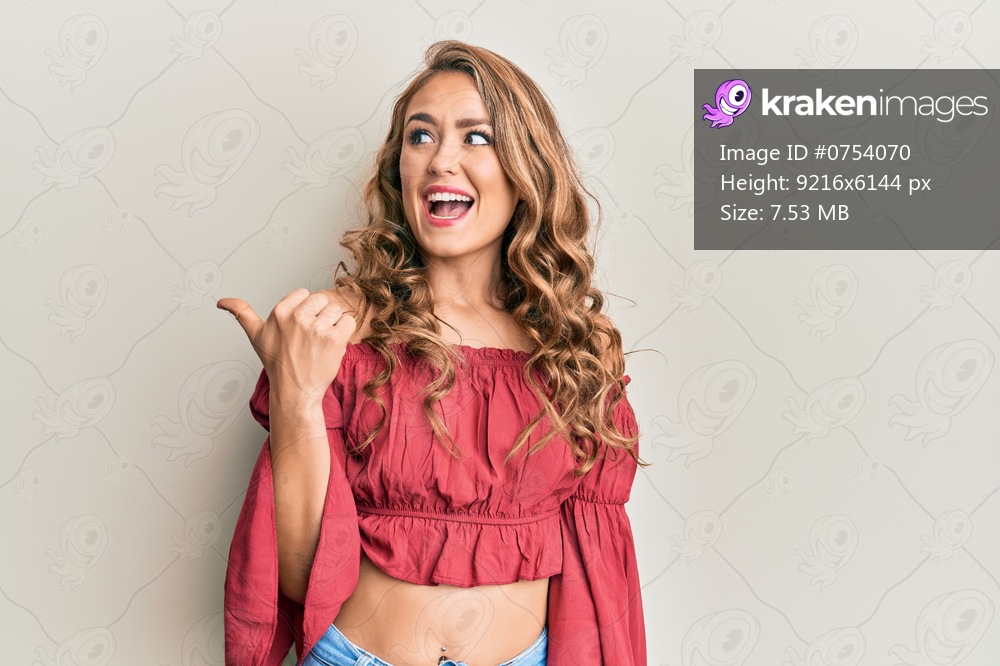 Young blonde girl wearing casual clothes pointing thumb up to the side smiling happy with open mouth 