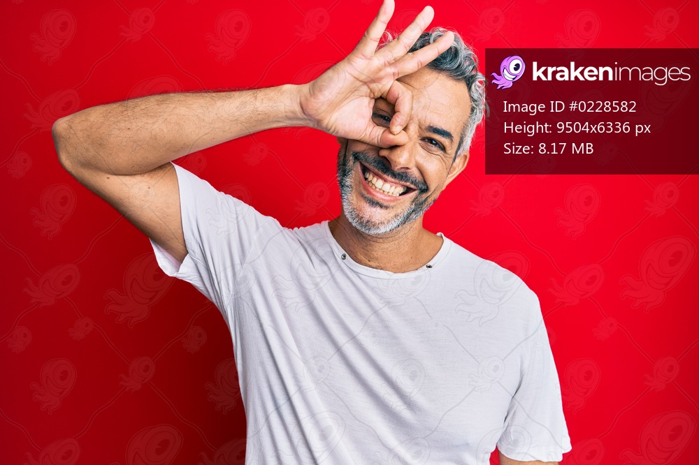 Middle age grey-haired man wearing casual white tshirt smiling happy doing ok sign with hand on eye looking through fingers 