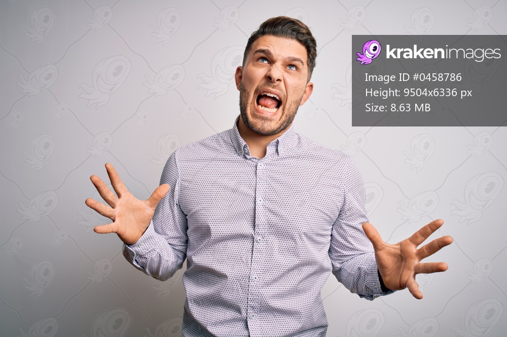 Young business man with blue eyes standing over isolated background crazy and mad shouting and yelling with aggressive expression and arms raised. Frustration concept.