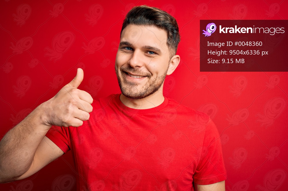 Young man with blue eyes wearing casual t-shirt over red isolated background doing happy thumbs up gesture with hand. Approving expression looking at the camera showing success.