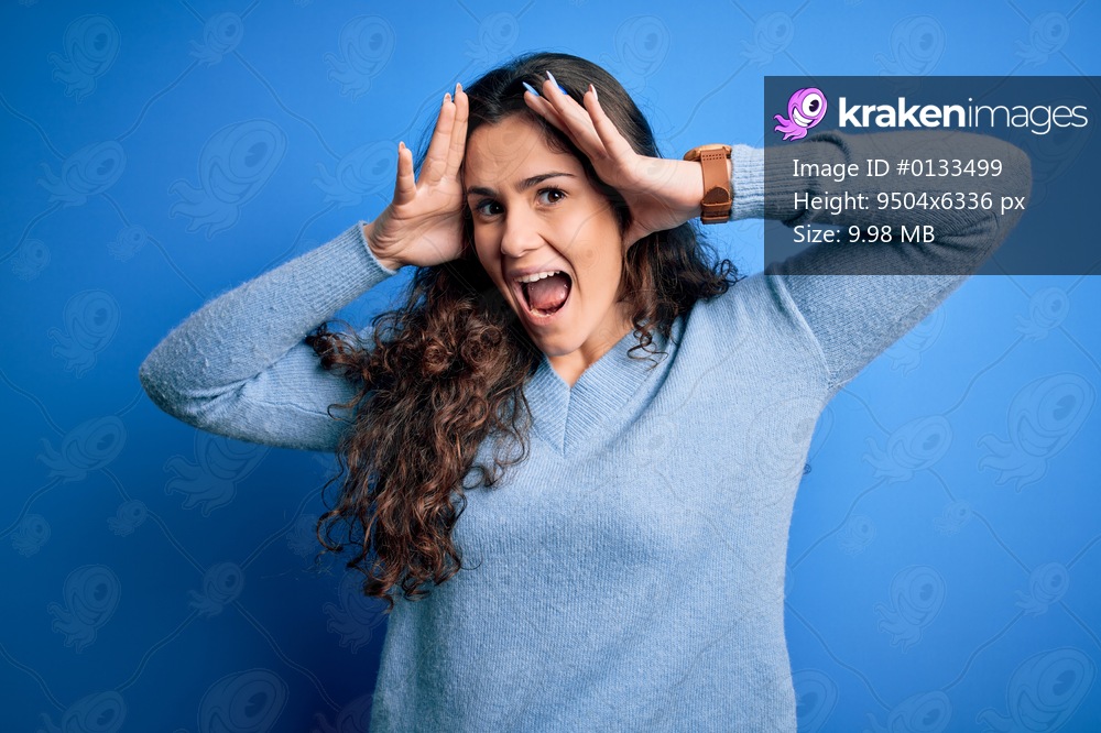 Young beautiful woman with curly hair wearing blue casual sweater over isolated background Smiling cheerful playing peek a boo with hands showing face. Surprised and exited