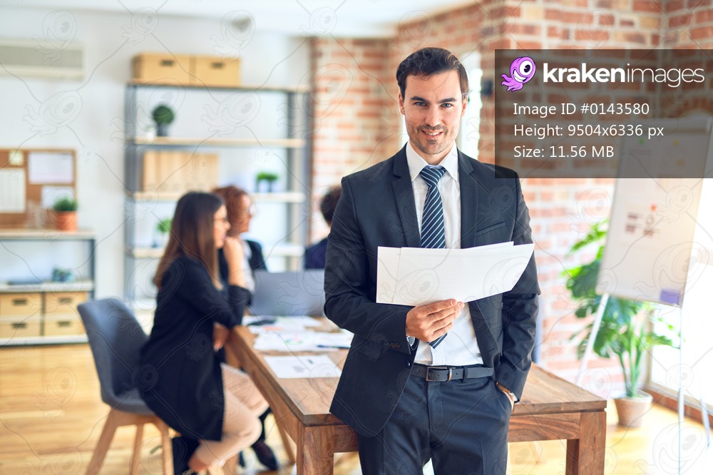 Group of business workers smiling happy and confident working together in a meeting. One of them, standing with smile on face reading documents at the office.