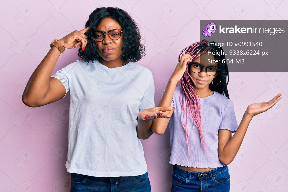 Beautiful african american mother and daughter wearing casual clothes and glasses confused and annoyed with open palm showing copy space and pointing finger to forehead. think about it. 