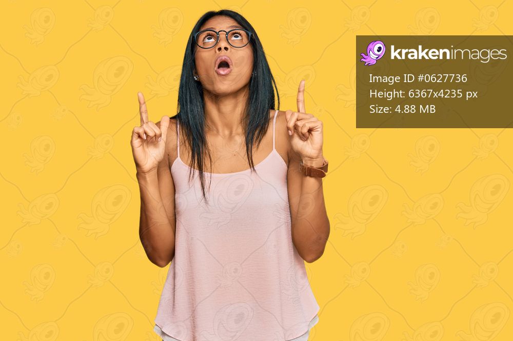 Young african american woman wearing casual clothes and glasses amazed and surprised looking up and pointing with fingers and raised arms. 