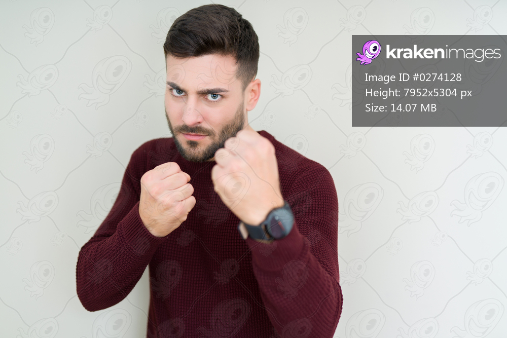 Young handsome man wearing a sweater over isolated background Ready to fight with fist defense gesture, angry and upset face, afraid of problem