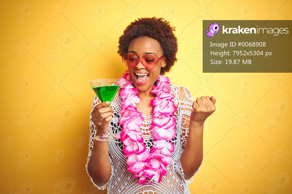 Young african american woman with afro hair wearing flower hawaiian lei and drinking a cocktail screaming proud and celebrating victory and success very excited, cheering emotion