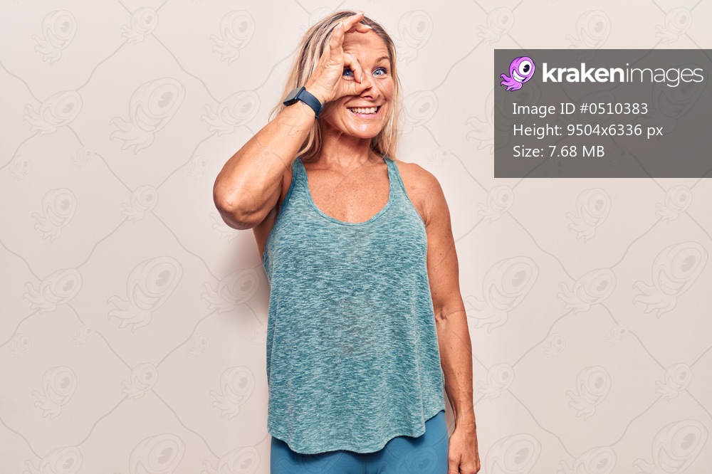 Middle age caucasian blonde woman wearing sportswear doing ok gesture with hand smiling, eye looking through fingers with happy face. 