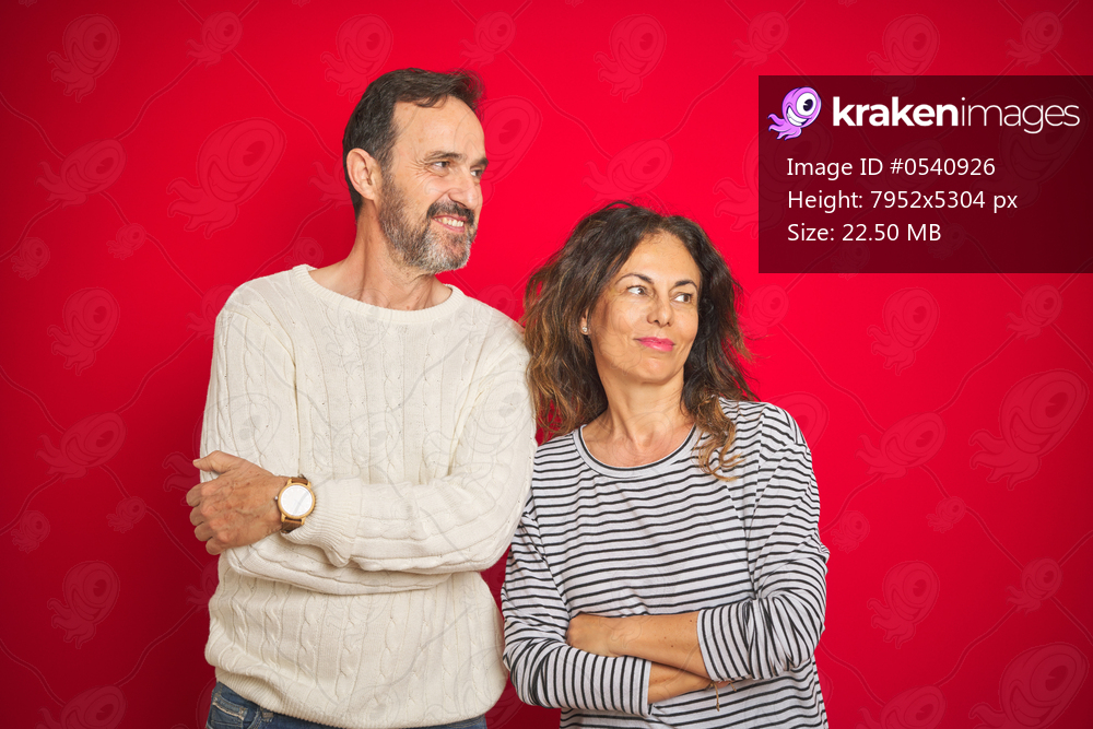 Beautiful middle age couple wearing winter sweater over isolated red background smiling looking to the side and staring away thinking.
