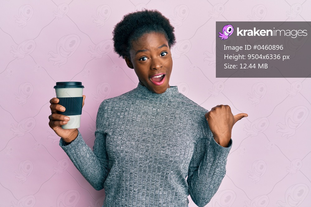 Young african american girl holding take away coffee pointing thumb up to the side smiling happy with open mouth 
