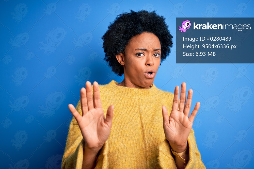 Young beautiful African American afro woman with curly hair wearing yellow casual sweater Moving away hands palms showing refusal and denial with afraid and disgusting expression. Stop and forbidden.