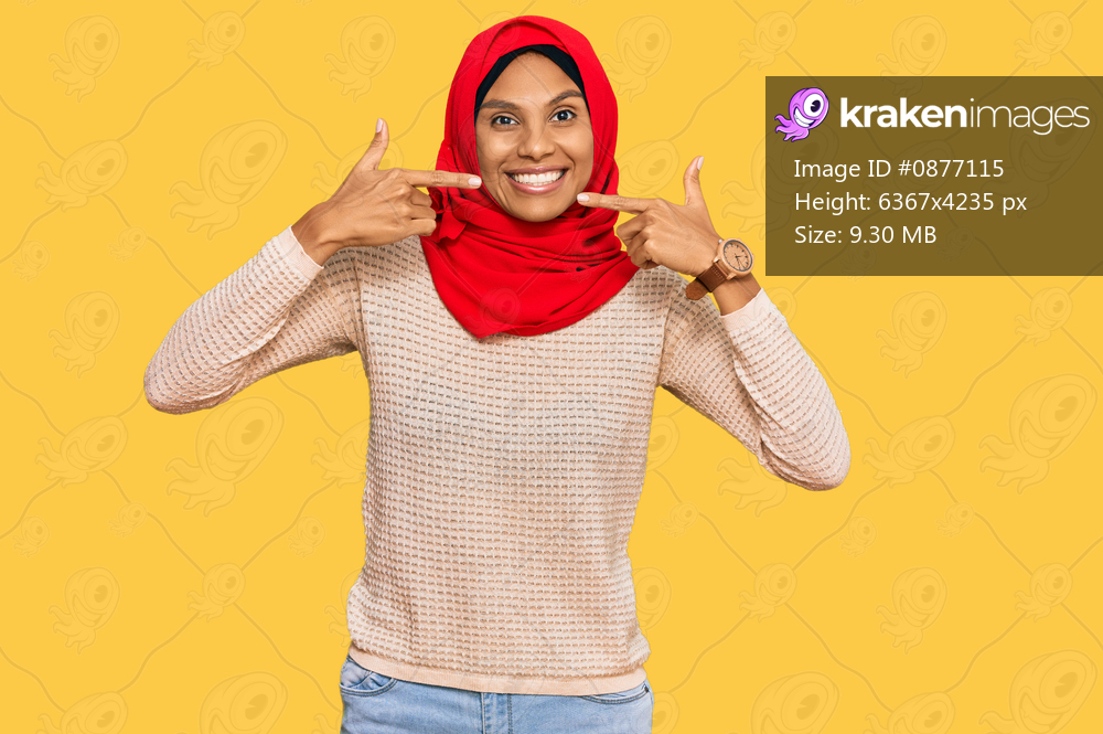 Young african american woman wearing traditional islamic hijab scarf smiling cheerful showing and pointing with fingers teeth and mouth. dental health concept. 