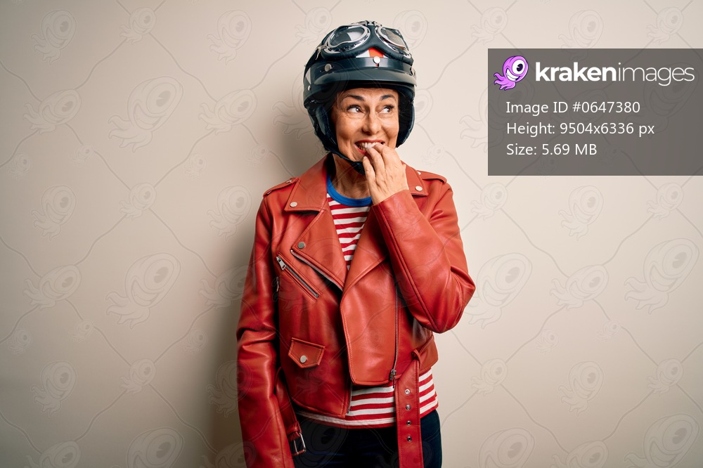 Middle age motorcyclist woman wearing motorcycle helmet and jacket over white background looking stressed and nervous with hands on mouth biting nails. Anxiety problem.