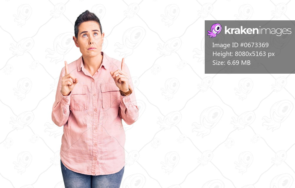 Young woman with short hair wearing casual clothes pointing up looking sad and upset, indicating direction with fingers, unhappy and depressed. 