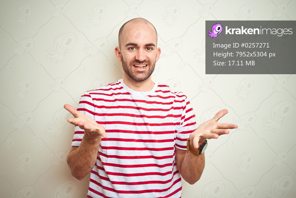 Young bald man with beard wearing casual striped red t-shirt over white isolated background smiling cheerful offering hands giving assistance and acceptance.