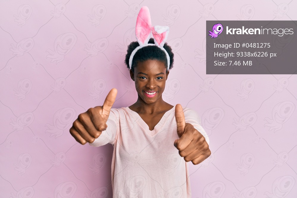 Young african american girl wearing cute easter bunny ears approving doing positive gesture with hand, thumbs up smiling and happy for success. winner gesture. 