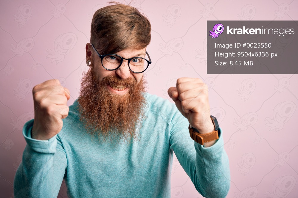 Handsome Irish redhead man with beard wearing glasses over pink isolated background angry and mad raising fists frustrated and furious while shouting with anger. Rage and aggressive concept.