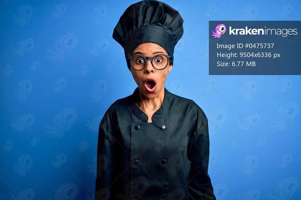 Young african american chef woman wearing cooker uniform and hat over blue background afraid and shocked with surprise and amazed expression, fear and excited face.
