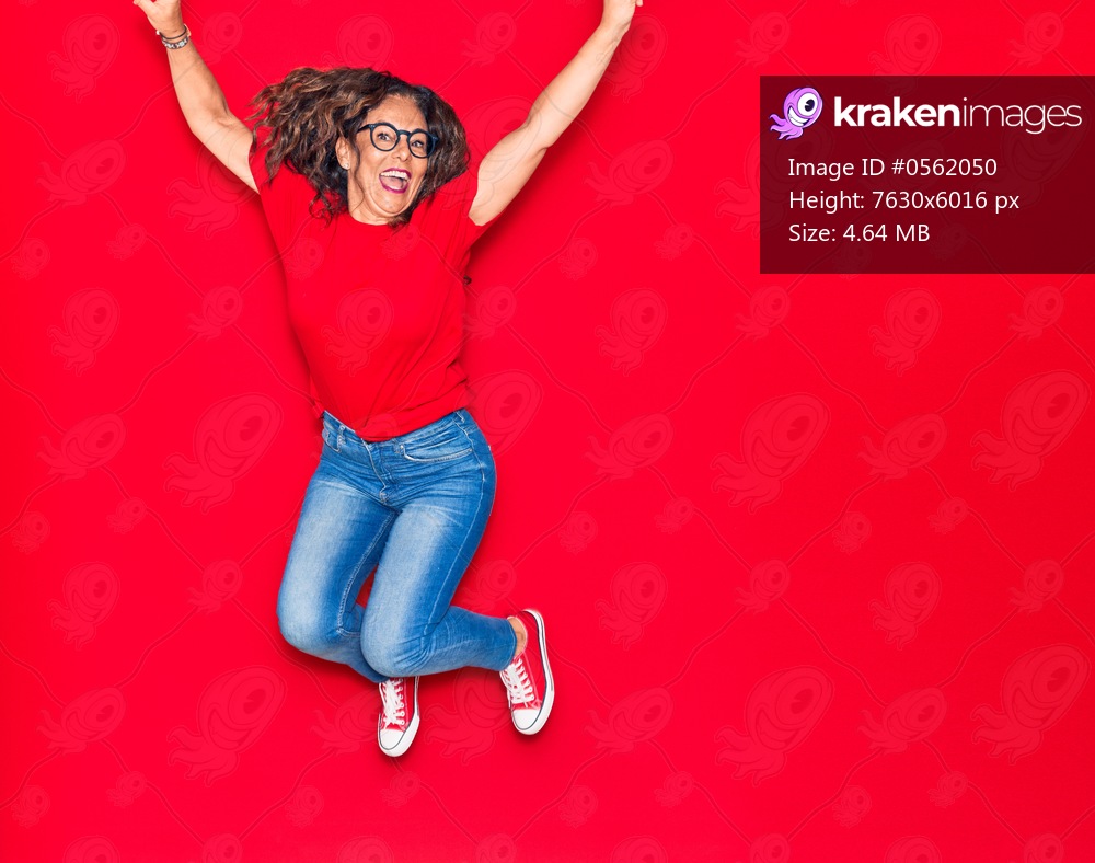 Middle age beautiful hispanic woman wearing casual clothes and glasses smiling happy. Jumping with smile on face over isolated red background
