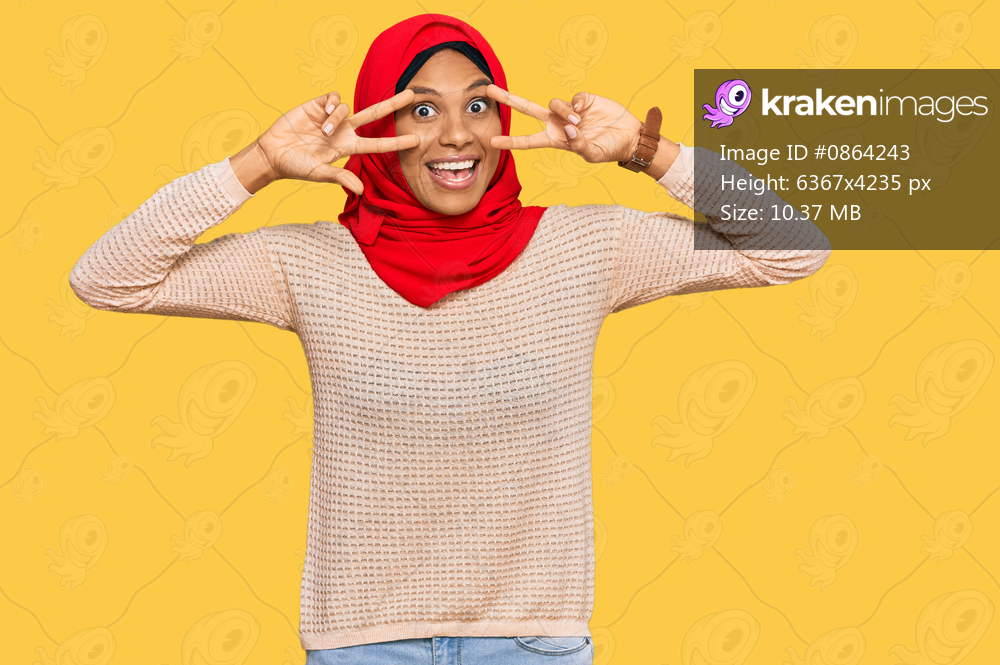 Young african american woman wearing traditional islamic hijab scarf doing peace symbol with fingers over face, smiling cheerful showing victory 