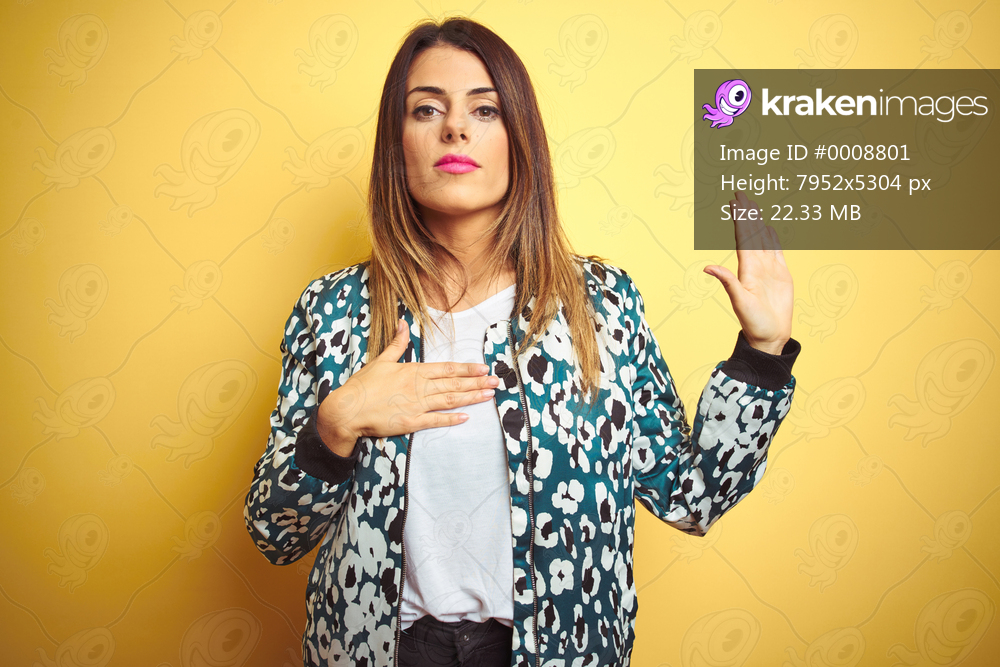 Young beautiful woman wearing casual jacket over yellow isolated background Swearing with hand on chest and open palm, making a loyalty promise oath