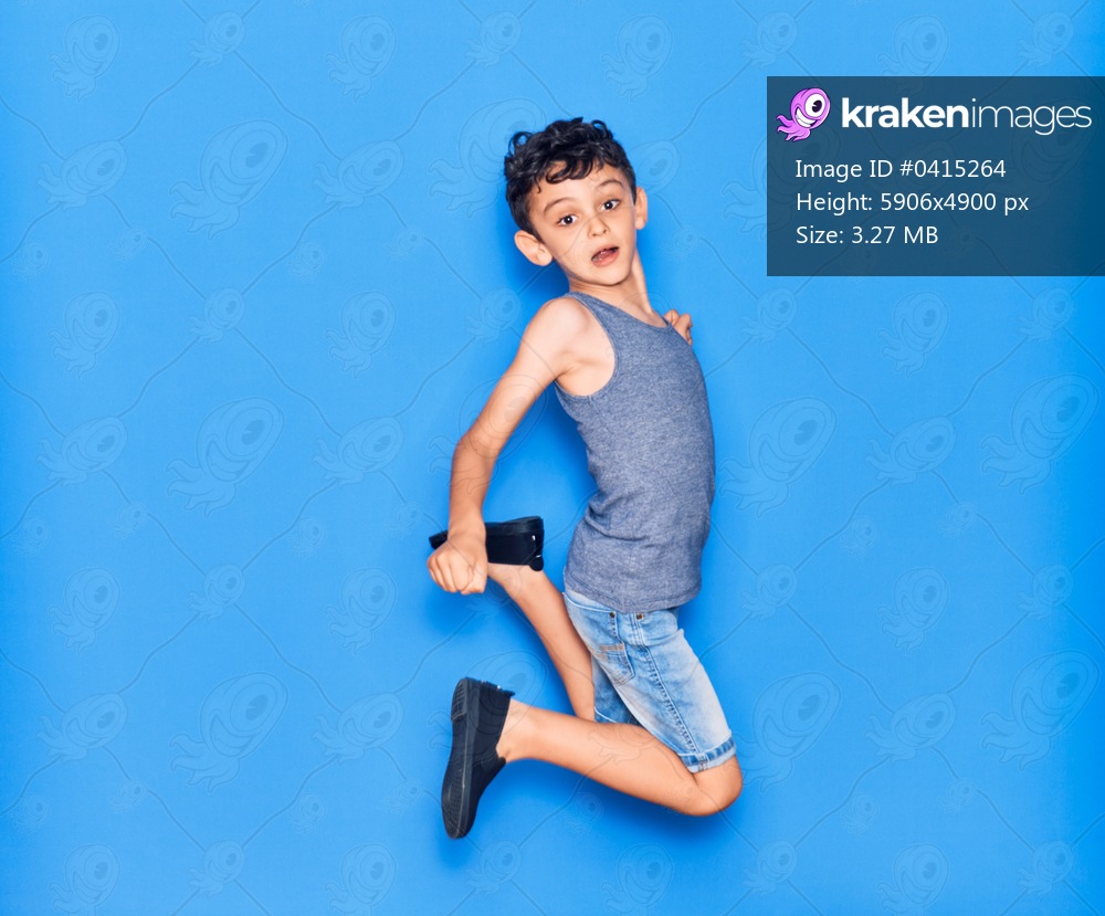 Adorable kid wearing casual clothes jumping over isolated blue background