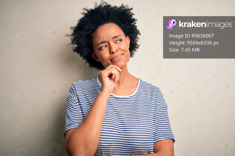 Young beautiful African American afro woman with curly hair wearing striped t-shirt with hand on chin thinking about question, pensive expression. Smiling with thoughtful face. Doubt concept.