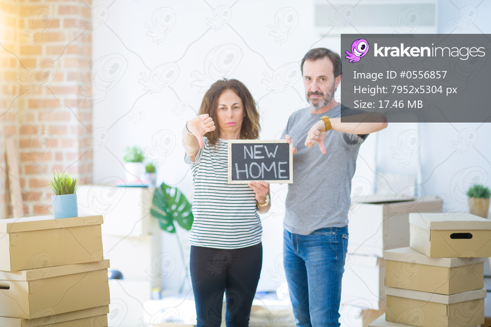 Middle age senior couple holding blackboard moving to a new home with angry face, negative sign showing dislike with thumbs down, rejection concept