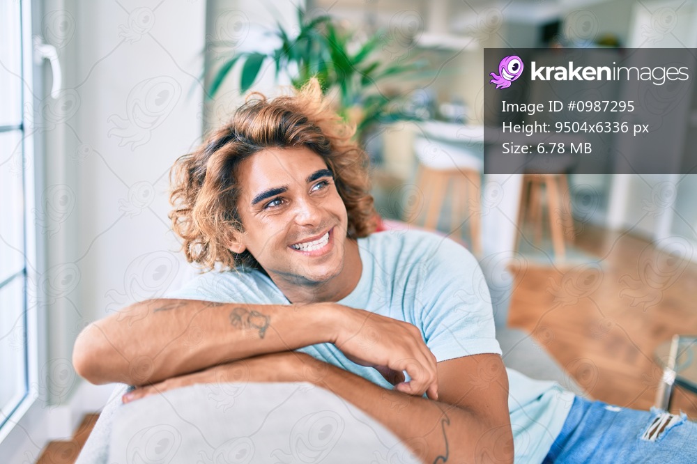 Young hispanic man smiling happy sitting on the sofa at home