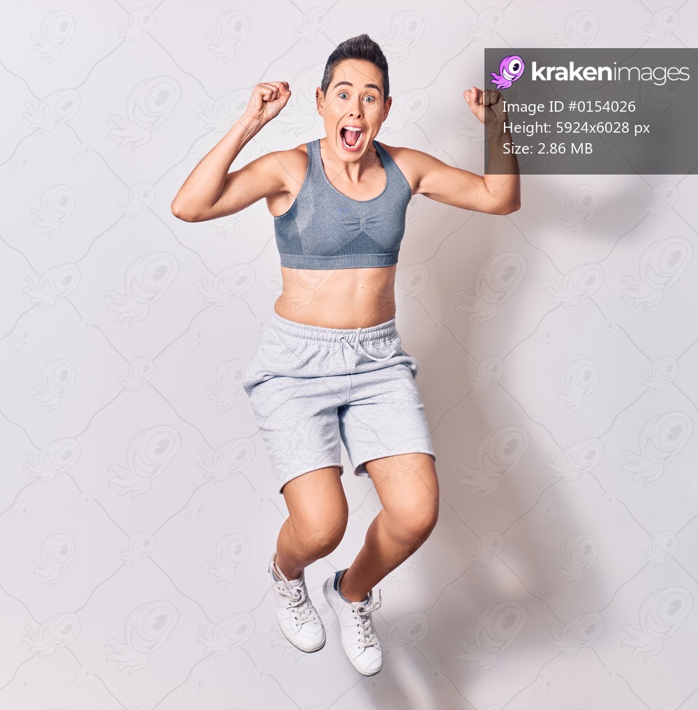Young beautiful caucasian sportswoman wearing sportswear smiling happy. Jumping with smile on face over isolated white background