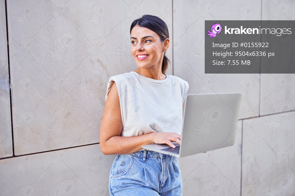 Beautiful young woman wearing fashionable clothes walking down the street and working using computer laptop