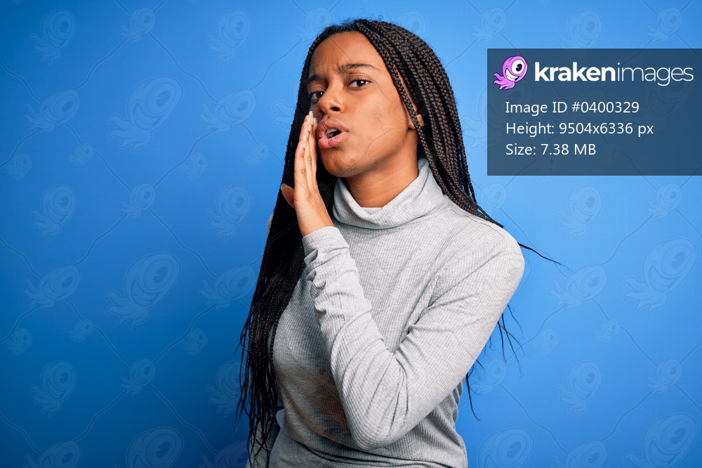 Young african american woman standing wearing casual turtleneck over blue isolated background hand on mouth telling secret rumor, whispering malicious talk conversation