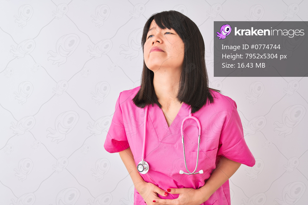 Young beautiful Chinese nurse woman wearing stethoscope over isolated white background with hand on stomach because indigestion, painful illness feeling unwell. Ache concept.