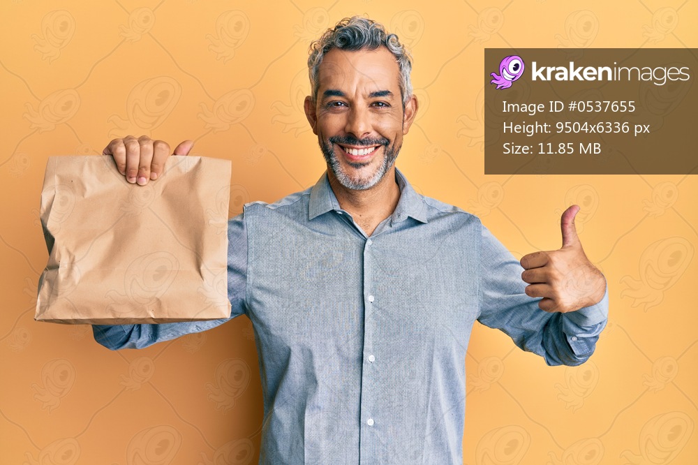 Middle age grey-haired man holding take away paper bag smiling happy and positive, thumb up doing excellent and approval sign 