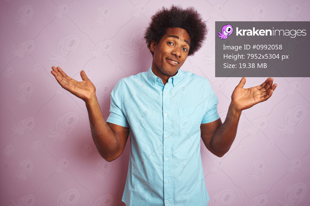 Young american man with afro hair wearing blue shirt standing over isolated pink background clueless and confused expression with arms and hands raised. Doubt concept.