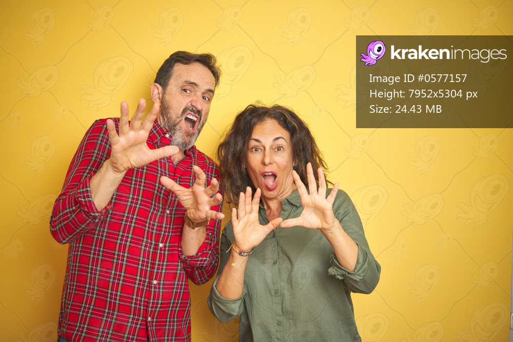 Beautiful middle age couple over isolated yellow background afraid and terrified with fear expression stop gesture with hands, shouting in shock. Panic concept.
