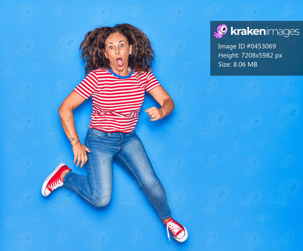 Middle age beautiful hispanic woman wearing casual clothes smiling happy. Jumping with smile on face over isolated blue background