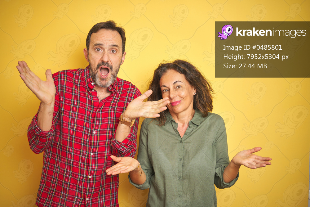 Beautiful middle age couple over isolated yellow background clueless and confused expression with arms and hands raised. Doubt concept.