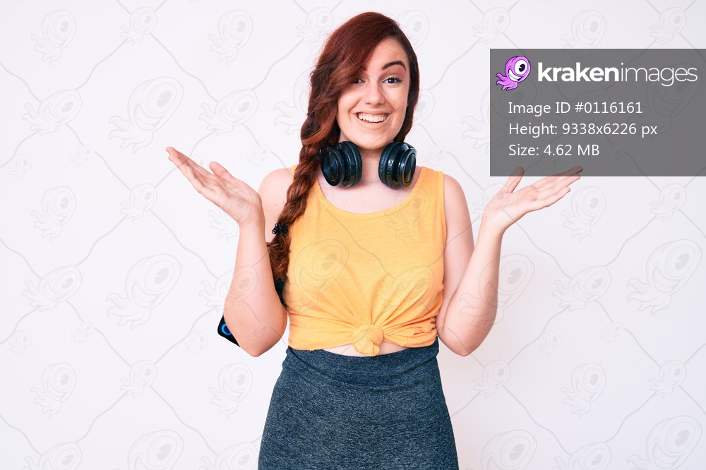 Young beautiful woman wearing gym clothes and using headphones celebrating victory with happy smile and winner expression with raised hands 