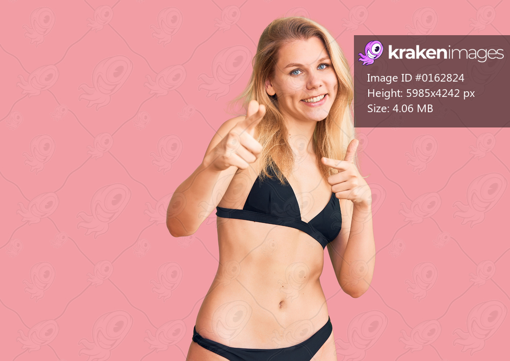 Young beautiful blonde woman wearing bikini pointing fingers to camera with happy and funny face. good energy and vibes. 