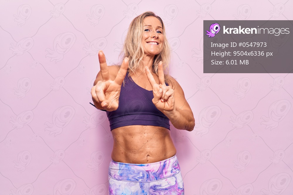 Middle age caucasian blonde woman wearing sportswear over pink background smiling looking to the camera showing fingers doing victory sign. number two. 