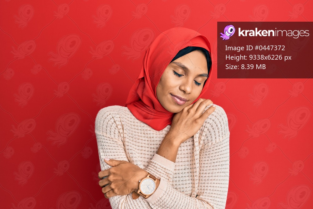 Young african american woman wearing traditional islamic hijab scarf hugging oneself happy and positive, smiling confident. self love and self care 