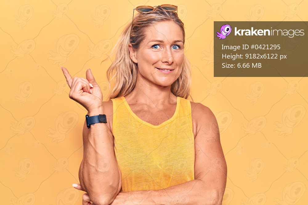 Middle age caucasian blonde woman wearing casual summer clothes and sunglasses smiling happy pointing with hand and finger to the side 