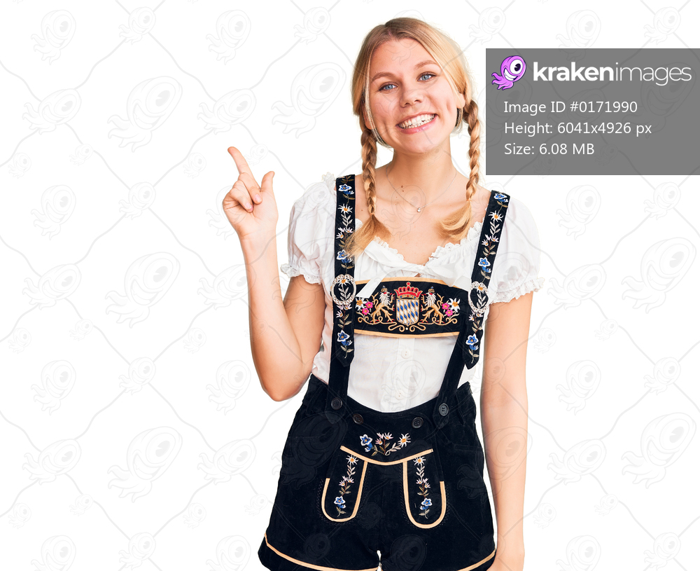 Young beautiful blonde woman wearing oktoberfest dress with a big smile on face, pointing with hand finger to the side looking at the camera. 