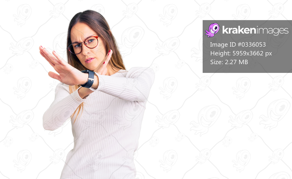 Beautiful brunette young woman wearing casual white sweater and glasses rejection expression crossing arms doing negative sign, angry face 