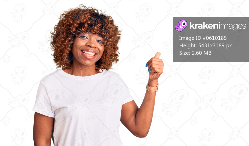 Young african american woman wearing casual white tshirt smiling with happy face looking and pointing to the side with thumb up. 