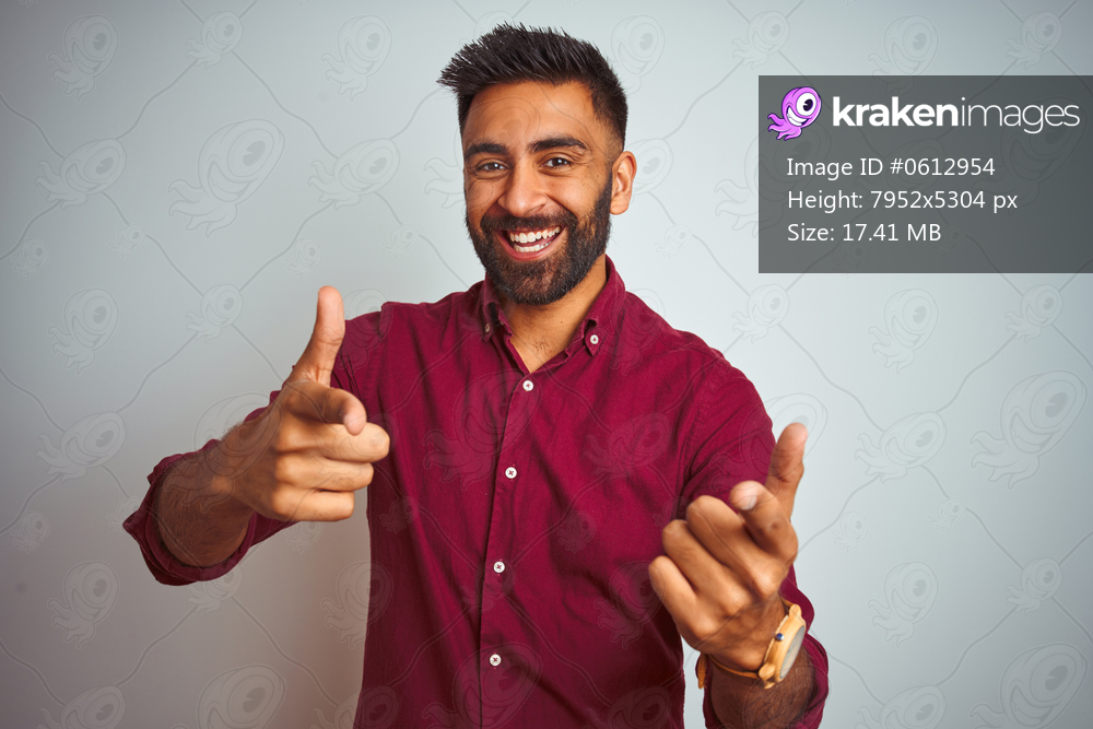 Young indian man wearing red elegant shirt standing over isolated grey background pointing fingers to camera with happy and funny face. Good energy and vibes.