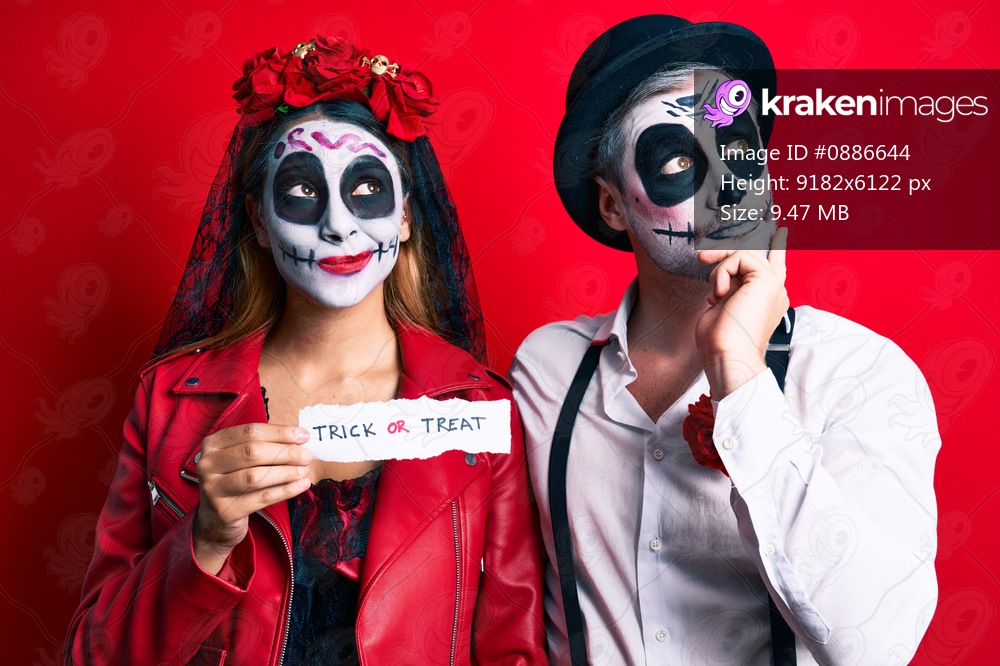 Couple wearing day of the dead costume holding trick or treat paper serious face thinking about question with hand on chin, thoughtful about confusing idea 