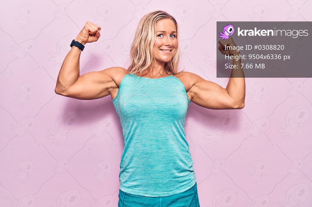 Middle age caucasian blonde woman wearing sports clothes over pink background showing arms muscles smiling proud. fitness concept. 