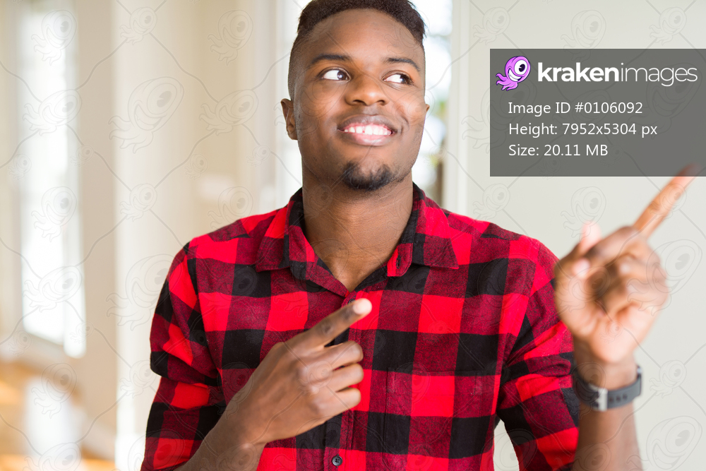 Handsome african american man smiling and looking at the camera pointing with two hands and fingers to the side.